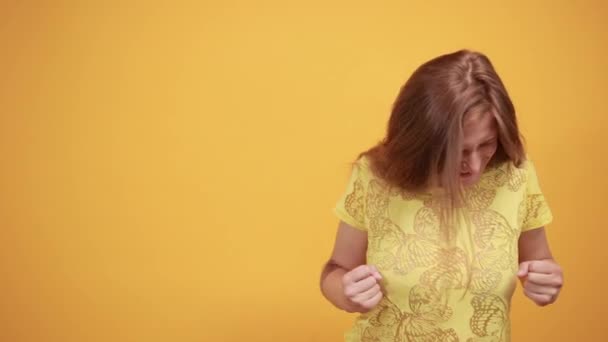 Brünettes Mädchen in gelbem T-Shirt über orangefarbenem Hintergrund zeigt Emotionen — Stockvideo