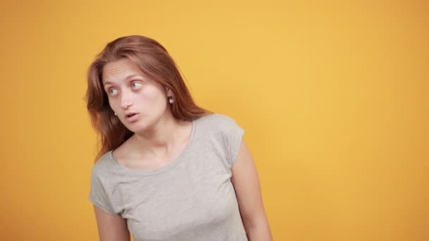 Brunette fille en gris t-shirt sur fond orange isolé montre des émotions — Video