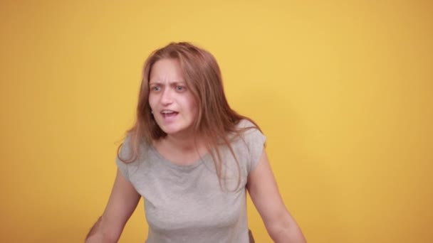 Brunetka v šedém tričku nad ojedinělým oranžovým pozadím vykazuje emoce — Stock video