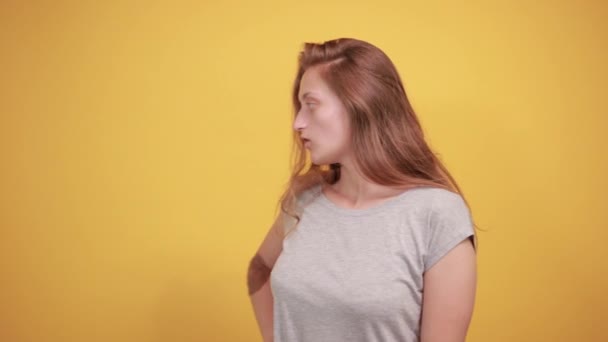 孤立したオレンジの背景の上に灰色のTシャツのブルネットの女の子は感情を示しています — ストック動画
