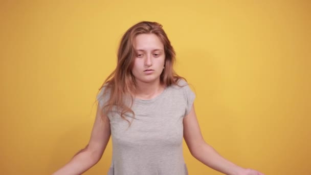 孤立したオレンジの背景の上に灰色のTシャツのブルネットの女の子は感情を示しています — ストック動画