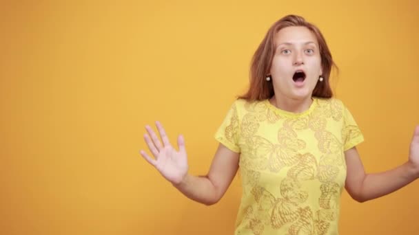 Brunette meisje in geel t-shirt over geïsoleerde oranje achtergrond toont emoties — Stockvideo