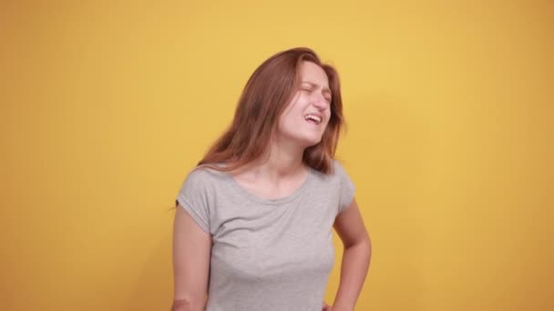 Brunette meisje in grijs t-shirt over geïsoleerde oranje achtergrond toont emoties — Stockvideo