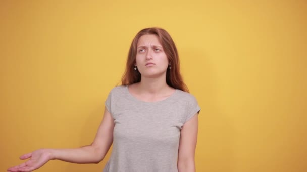 Брюнетка дівчина в сірій футболці над ізольованим помаранчевим тлом показує емоції — стокове відео