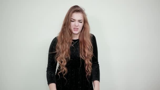 Fille aux cheveux bruns en robe noire sur fond blanc isolé montre des émotions — Video