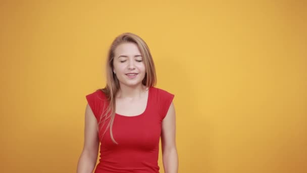 Gadis muda berambut pirang dengan kaos merah di atas latar belakang oranye yang terisolasi menunjukkan emosi — Stok Video