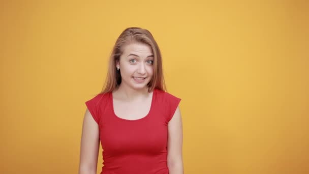 孤立したオレンジの背景の上に赤いTシャツの若いブロンドの女の子は感情を示しています — ストック動画