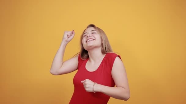 Jeune fille blonde en t-shirt rouge sur fond orange isolé montre des émotions — Video
