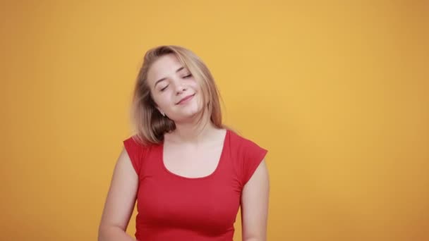 Jeune fille blonde en t-shirt rouge sur fond orange isolé montre des émotions — Video