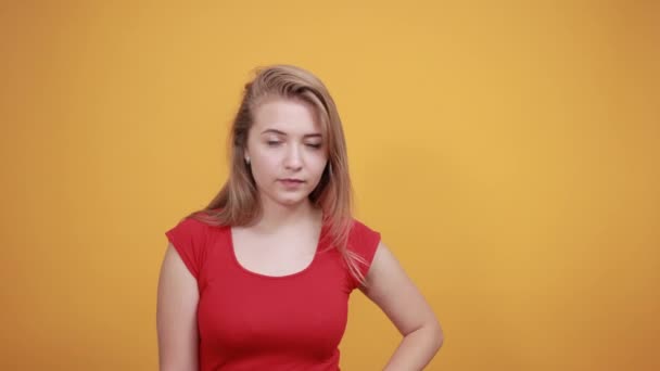 Giovane ragazza bionda in t-shirt rossa su sfondo arancione isolato mostra emozioni — Video Stock