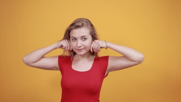 Jeune fille blonde en t-shirt rouge sur fond orange isolé montre des émotions — Video