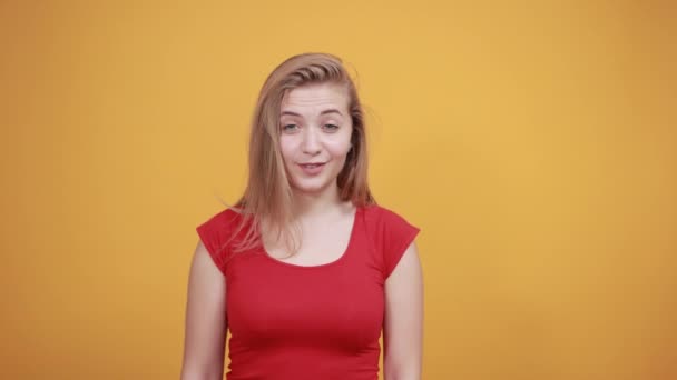 年轻的金发女孩在红色T恤在孤立的橙色背景显示情感 — 图库视频影像