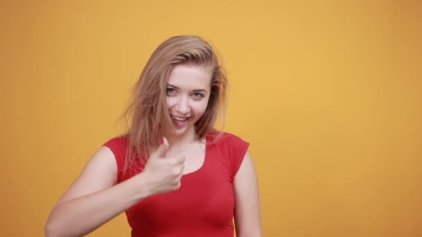 Jeune fille blonde en t-shirt rouge sur fond orange isolé montre des émotions — Video