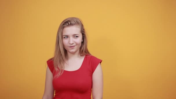 Jeune fille blonde en t-shirt rouge sur fond orange isolé montre des émotions — Video