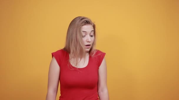 Νεαρή ξανθιά κορίτσι με κόκκινο μπλουζάκι πάνω από απομονωμένο πορτοκαλί φόντο δείχνει τα συναισθήματα — Αρχείο Βίντεο