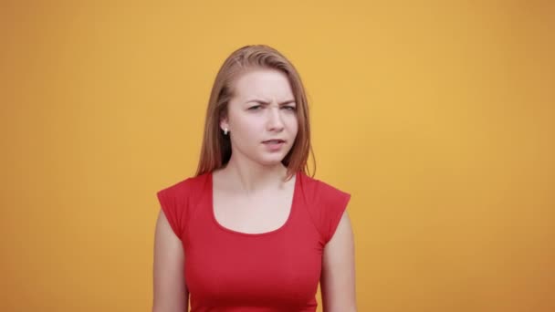 Νεαρή ξανθιά κορίτσι με κόκκινο μπλουζάκι πάνω από απομονωμένο πορτοκαλί φόντο δείχνει τα συναισθήματα — Αρχείο Βίντεο