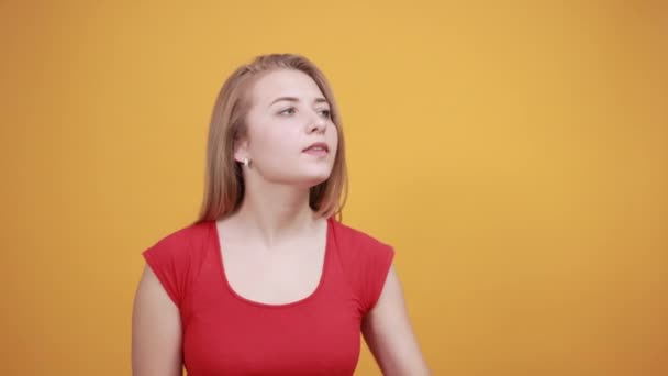 Молодая блондинка в красной футболке на изолированном оранжевом фоне показывает эмоции — стоковое видео