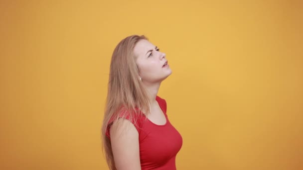 Jeune fille blonde en t-shirt rouge sur fond orange isolé montre des émotions — Video