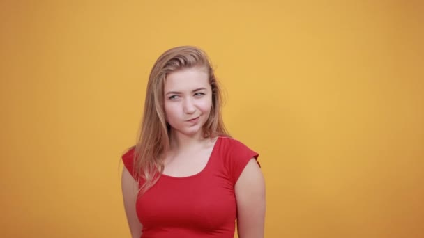 Jeune fille blonde en t-shirt rouge sur fond orange isolé montre des émotions — Video