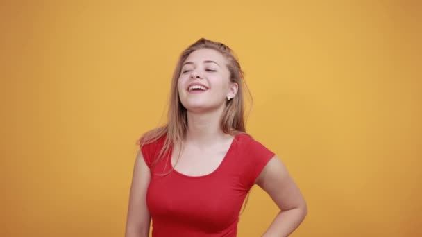 Jeune fille blonde en t-shirt rouge sur fond orange isolé montre des émotions — Video