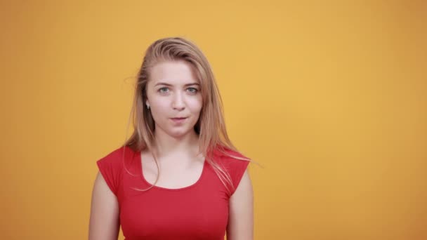 Jeune fille blonde en t-shirt rouge sur fond orange isolé montre des émotions — Video