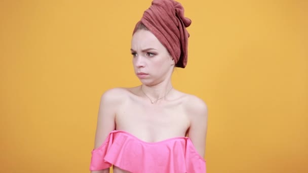 孤立したオレンジ色の背景の上に彼女の頭の上にタオルを持つ若い女の子は感情を示しています — ストック動画