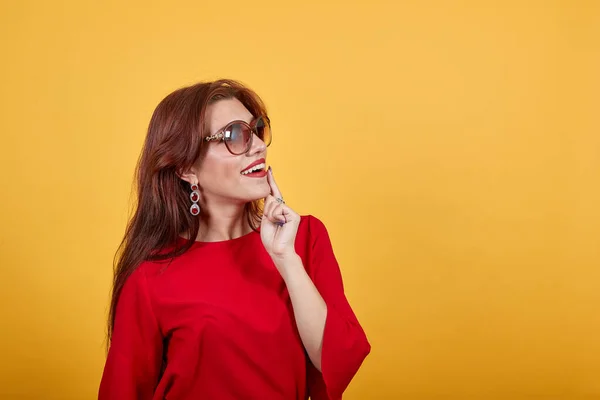 Mooie vrouw in zonnebril staan over gele muur en denken een idee. — Stockfoto