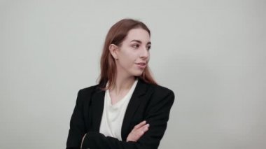 Ayakta duruyor ve kollarını göğsünde kavuşturuyor. Kahverengi saçlı, çekici bir kadın.