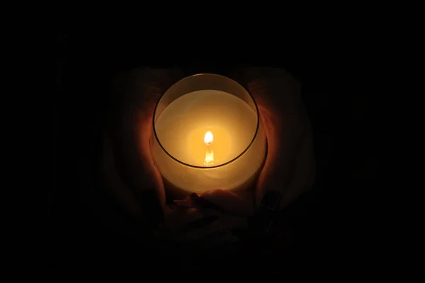 Burning candle in the hands in complete darkness.