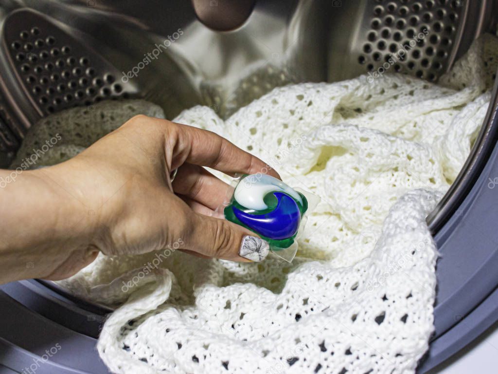 Girl's hand lays a capsule with a powder for washing white things.