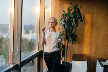 İş kadını pencerenin yanındaki ofiste duruyor ve belgeleri inceliyor. İş, finans, avukat