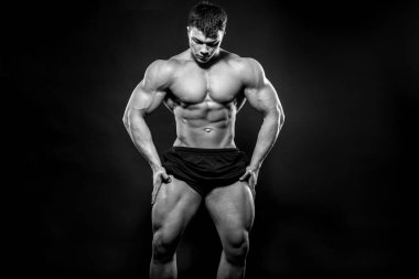 Stüdyoda siyah arka planda poz veren seksi genç bir atlet. Fitness, vücut geliştirme, siyah beyaz