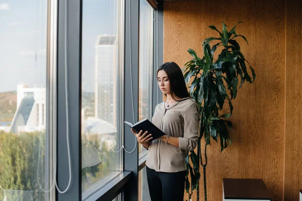 Business woman is standing in the office near the window and is studying documents. Business, finance, lawyer