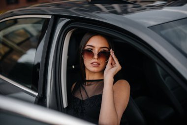 Siyah elbiseli, birinci sınıf bir arabada oturan şık bir genç kız. İş modası ve tarzı