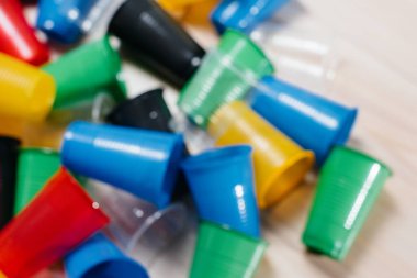 Zemine saçılmış geniş renkli plastik bardaklar yığını, odak dışı. Çevrenin insan atıklarıyla kirlenmesi