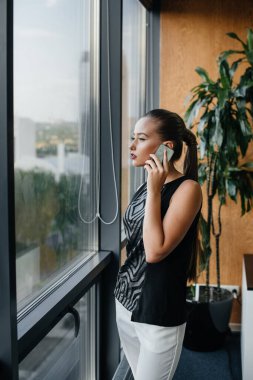 Sekreter, ofisin penceresinin yanında telefonla konuşuyor.