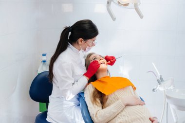 Profesyonel bir dişçi modern bir diş muayenehanesinde hamile bir kızın ağız boşluğunu tedavi eder ve muayene eder. Dişçilik