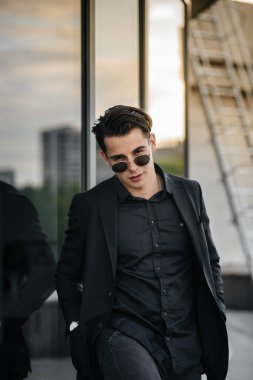 Şık bir genç adam gün batımında aynalı bir binanın yanında duruyor. Moda.