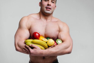 Parlak meyveli beyaz bir arka planda poz veren sportif seksi adam. Diyet olsun. Sağlıklı beslenme