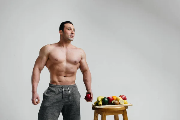 Sexy vegan guy with a naked torso posing in the Studio next to fruit. Diet. Healthy diet