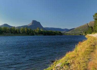 Güneşli bir yaz gününde, açık mavi gökyüzü ve Sorkjosen yakınlarındaki dağlara ve Reisaelva nehrine bakın.