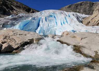 Güneşli bir yaz gününde Jostedalsbreen Ulusal Parkı 'nda açık mavi gökyüzü ile buzul Nigardsbreen' in dibine su sıçrıyor.