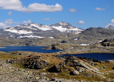Güneşli bir yaz gününde Jotunheimen Ulusal Parkı 'nın çorak arazisindeki göller ve buzullar açık mavi gökyüzü ve birkaç bulutla