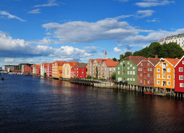 View from Gamle Bybru Bridge to the Coloured Wooden Waterfront of Bakklandet in Trondheim At The Nidelv River On A Sunny Summer Day With A Clear Blue Sky And A Few Clouds