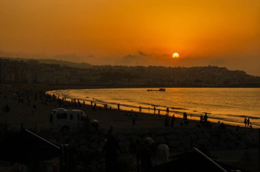 Kumsalda turuncu bir gün batımı ve binalar.