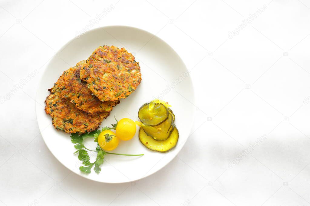 Zucchini patties on a white plate with pickles, tomatoes and cilantro.
