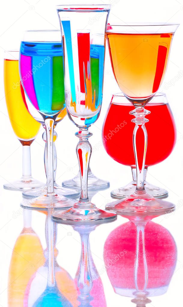 Glass goblets with colored drinks stand on a glass surface