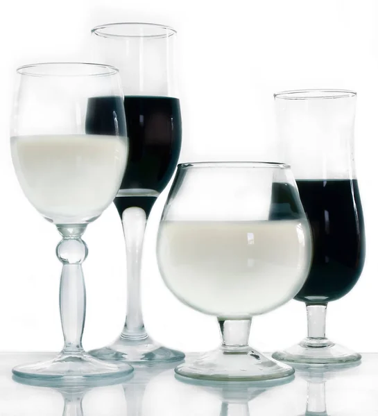 Glasses with white and black drinks on a white background and glass surface