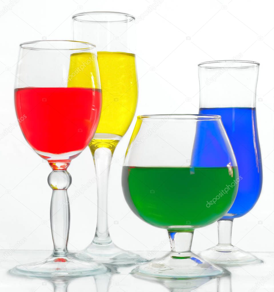 Wine glasses with yellow, blue, green and red liquid on a glass surface