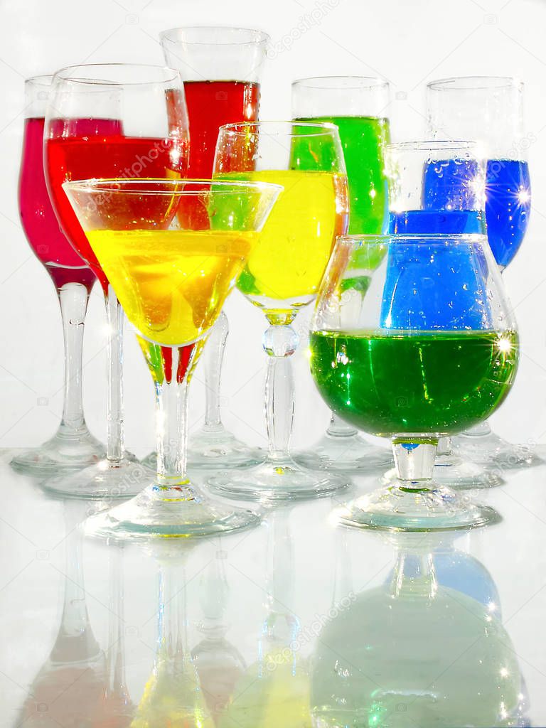 Wine glasses with red, blue, green, yellow liquids stand on a glass surface on a white background